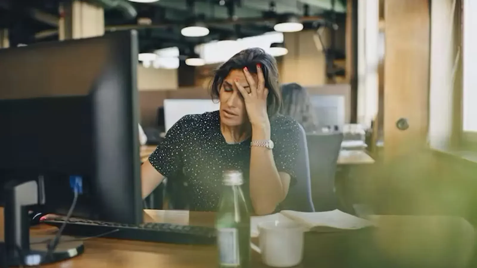 donna alla sua scrivania al lavoro tenendo la testa
