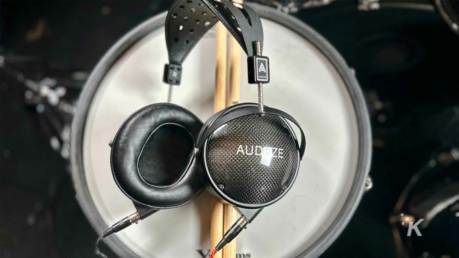 Um baterista toca um instrumento de percussão usando fones de ouvido e ouvindo música por meio de um alto-falante conectado a um equipamento de áudio com fones de ouvido Audeze.