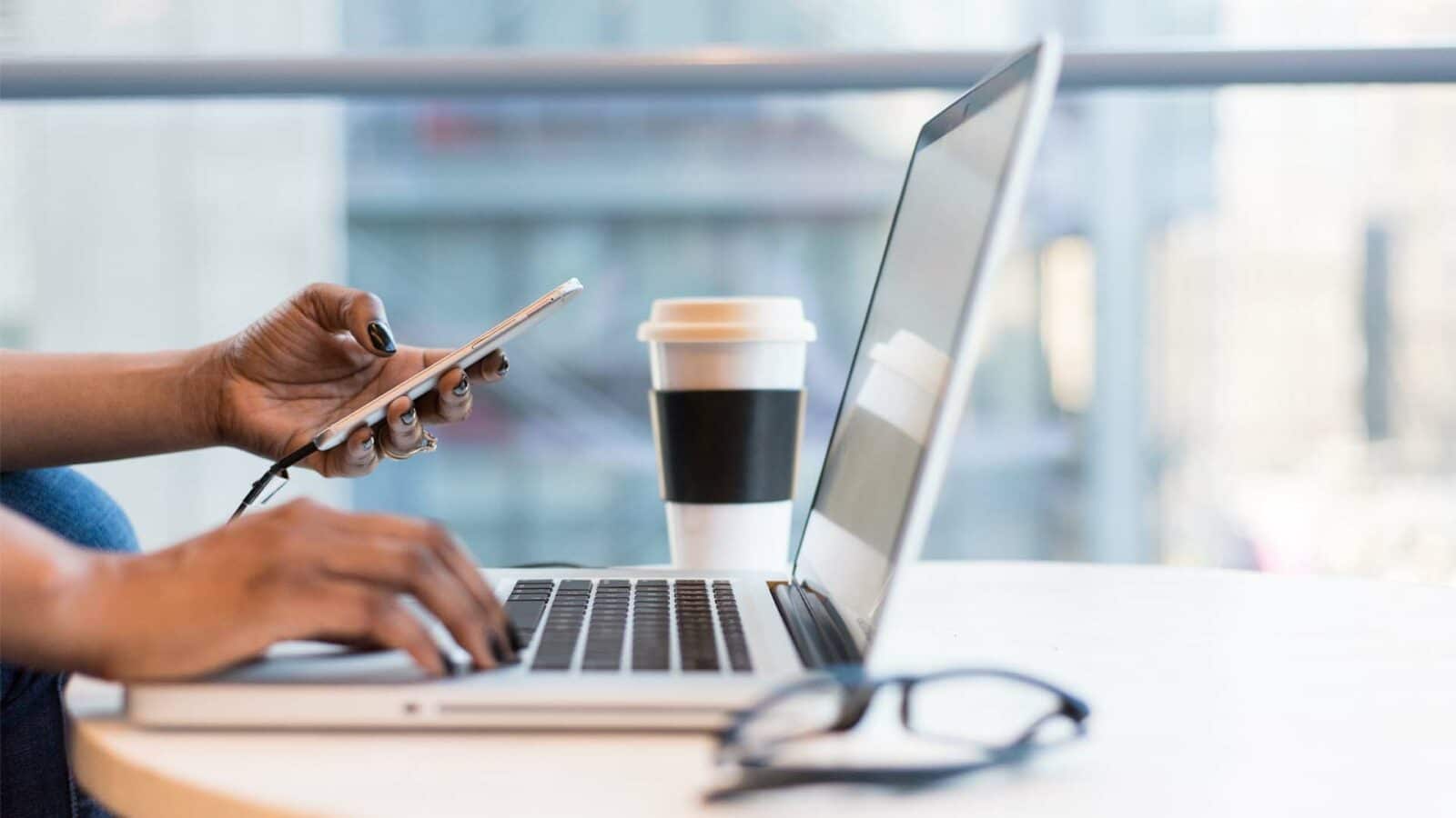 La persona sta utilizzando un laptop su un tavolo mentre sorseggia una tazza di caffè. Comunicazione interna