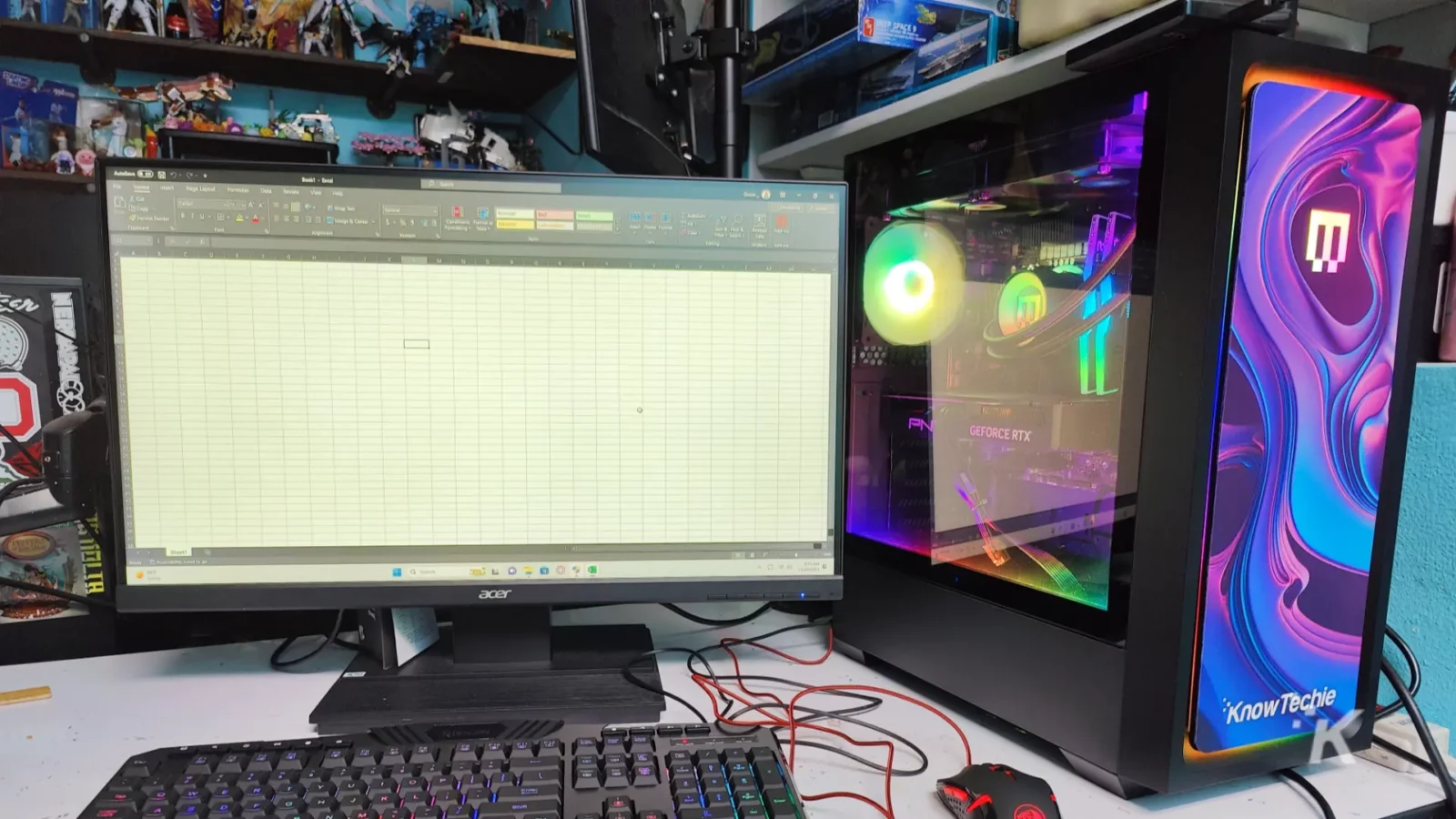 evaluando el excelente maingear mg-1 platinum The image shows a desk with a computer monitor displaying a spreadsheet, a backlit keyboard, a custom pc with rgb lighting, and various collectibles on shelves.