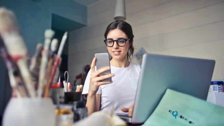 aplikasi seluler terbaik untuk pekerja lepas Freelancer looking at phone while working on laptop.