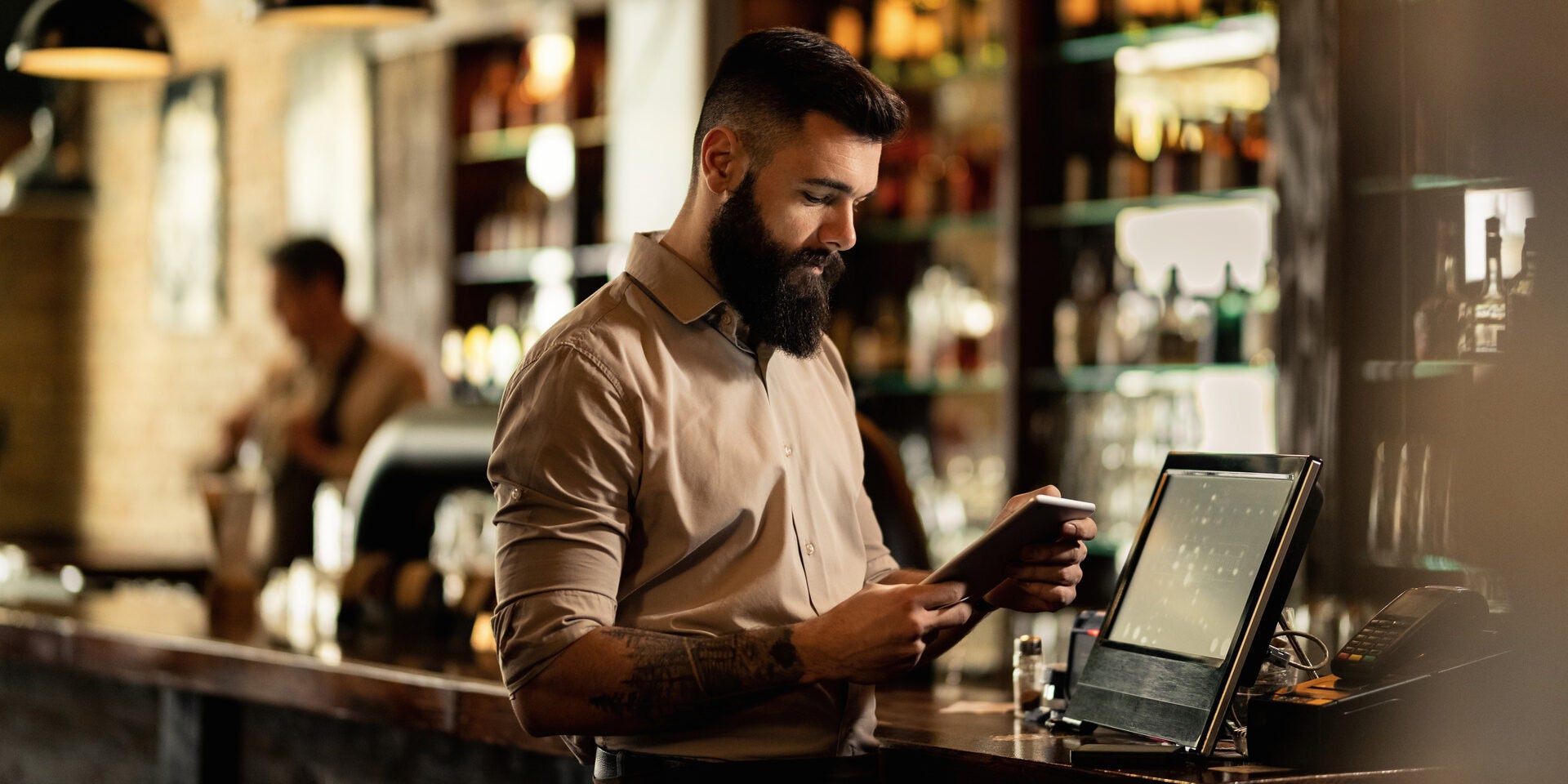 Un jeune barman barbu hipster utilise un système de point de vente au travail