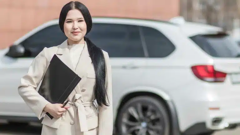 Wanita profesional dengan folder di samping mobil putih.