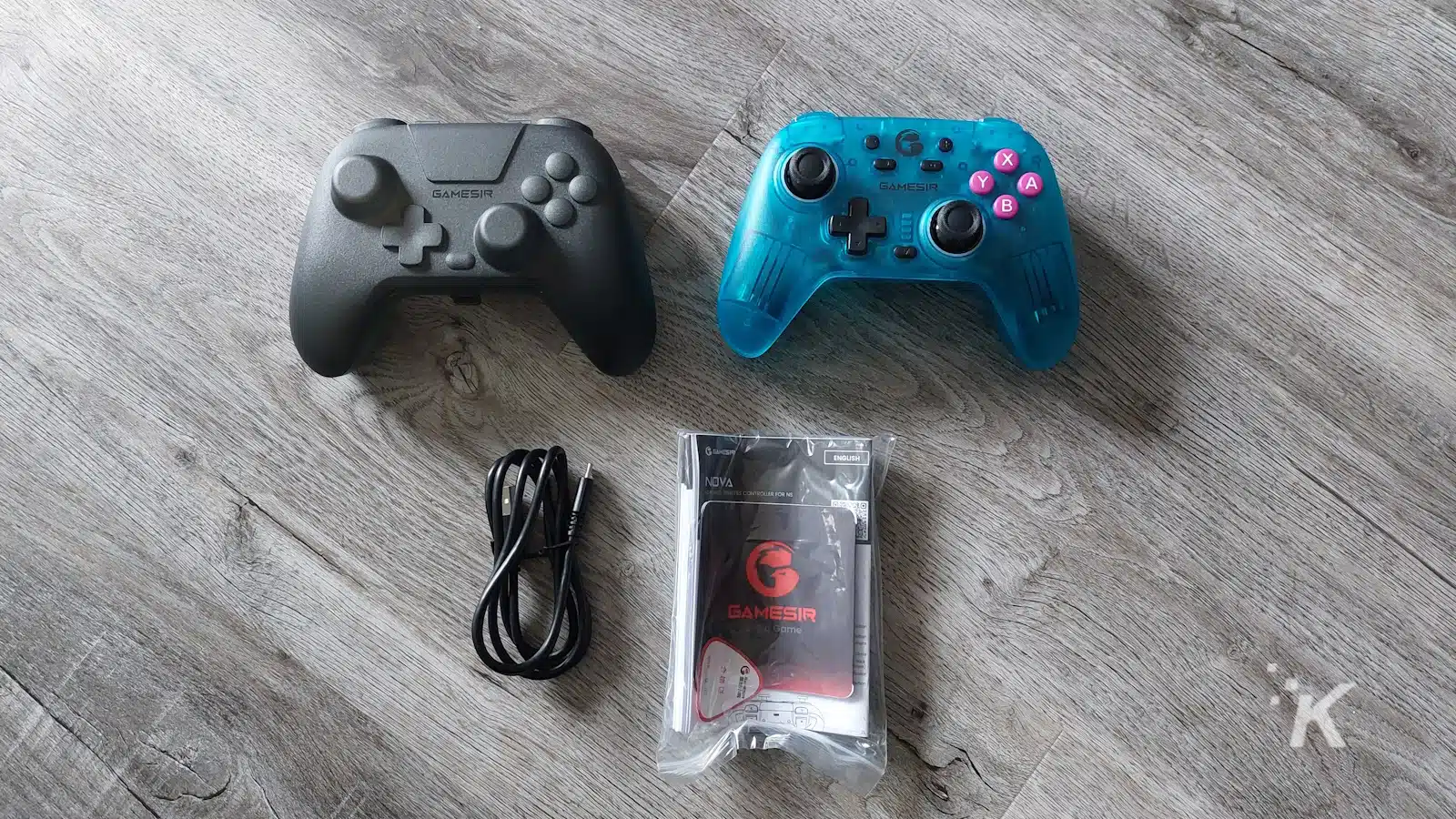 Două controlere GameSir și accesorii pe podea din lemn.
