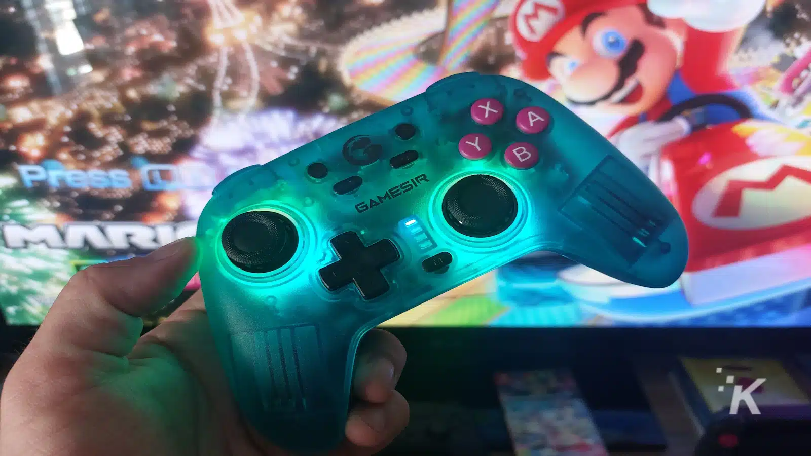 Controlerul Gamesir ținut în fața ecranului de joc Mario.