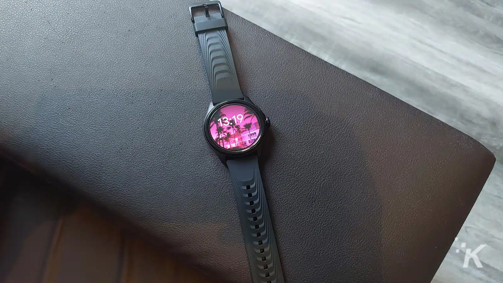 茶色の表面にヤシの木の壁紙が付いている黒いスマートウォッチ。