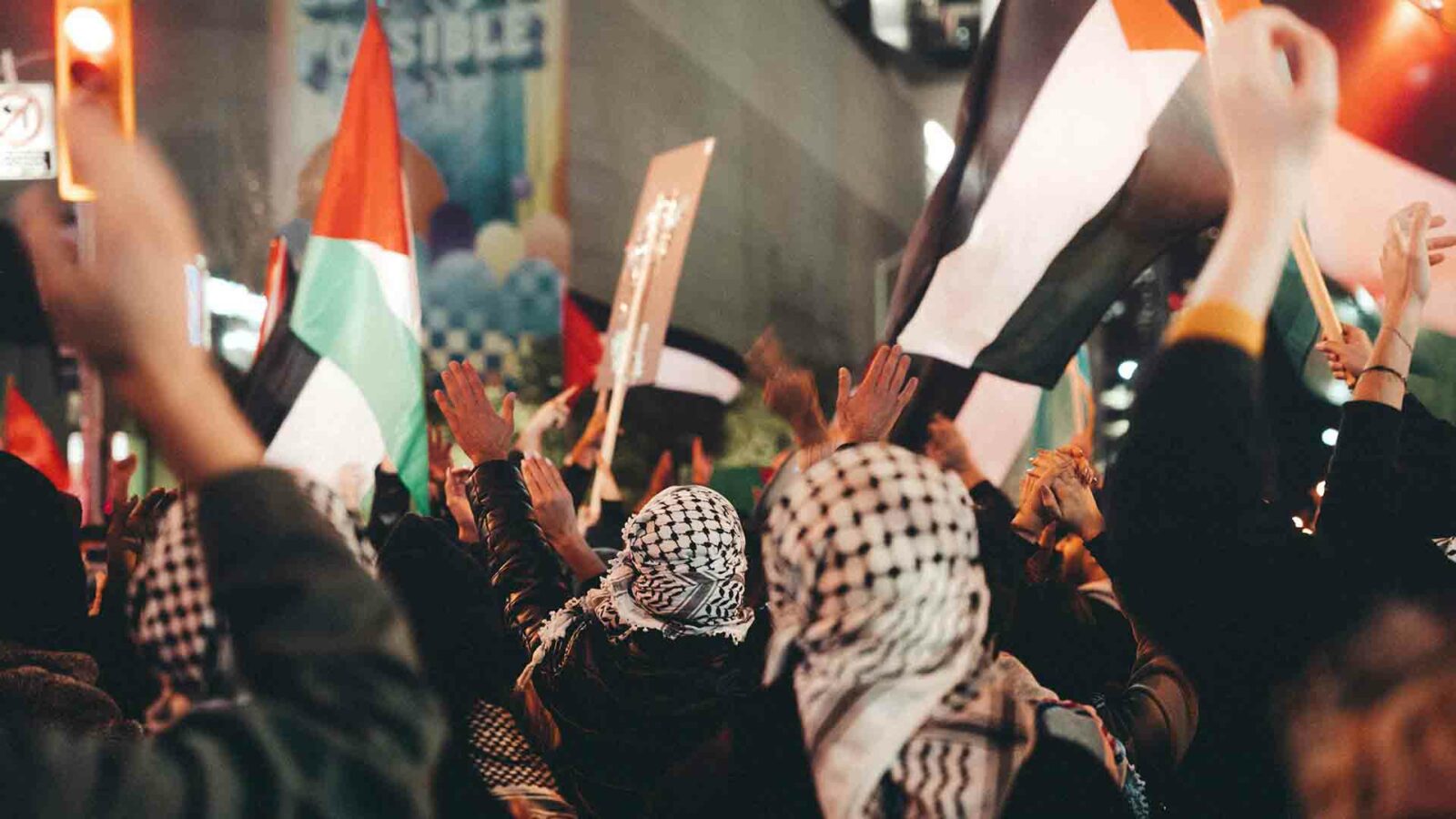 Manifestantes con banderas palestinas en una calle concurrida por la noche.