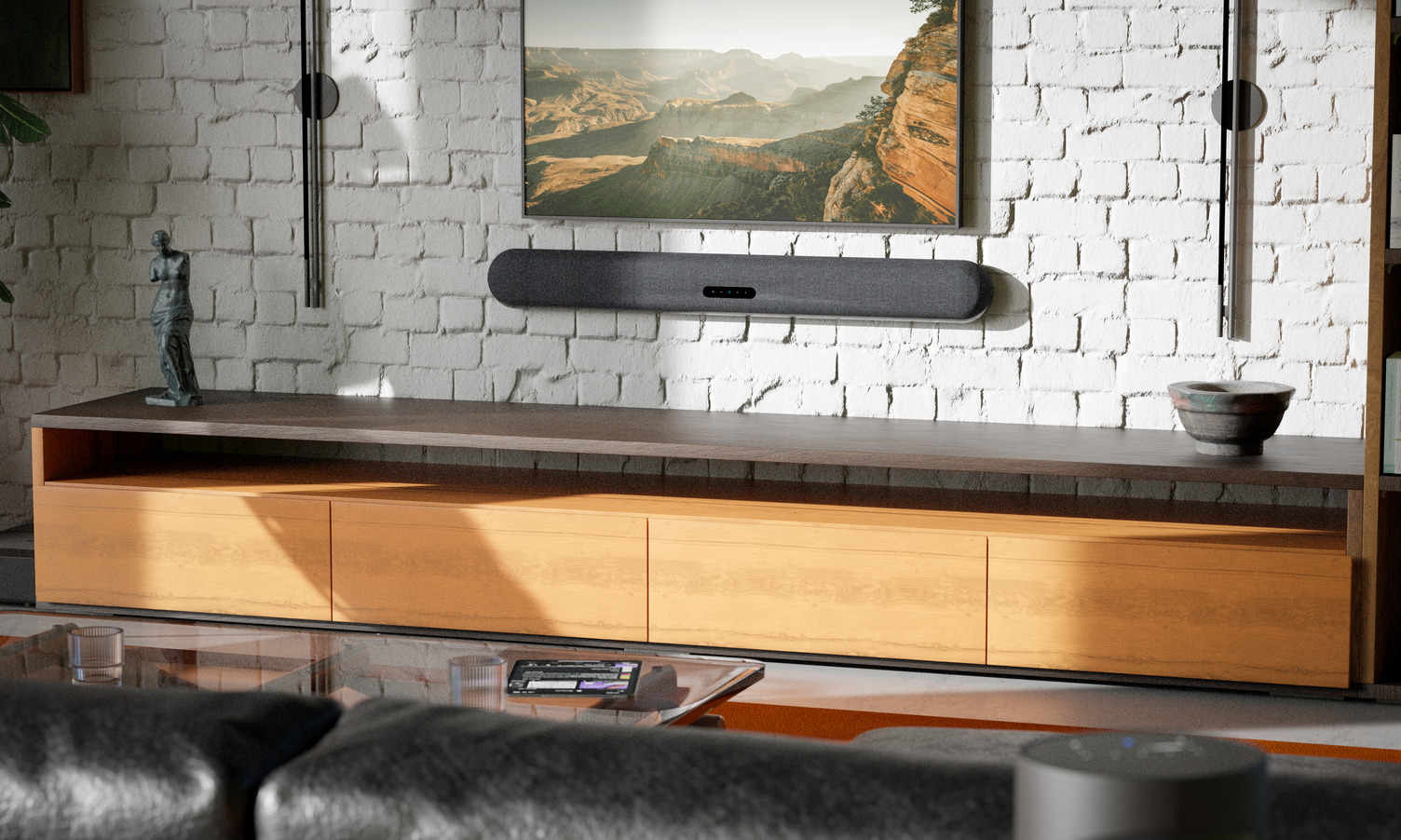 Lifestyle-Aufnahme des Bluesound-Puls-Kinos auf einer weißen Ziegelmauer unter einem mittelgroßen Fernseher und über einer hölzernen Unterhaltungseinheit